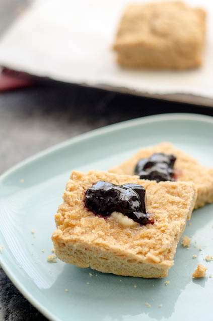 Square whole wheat biscuit  cut in half  on a blue plate  and topped with melting butter pat and a dollop of blackberry jam 