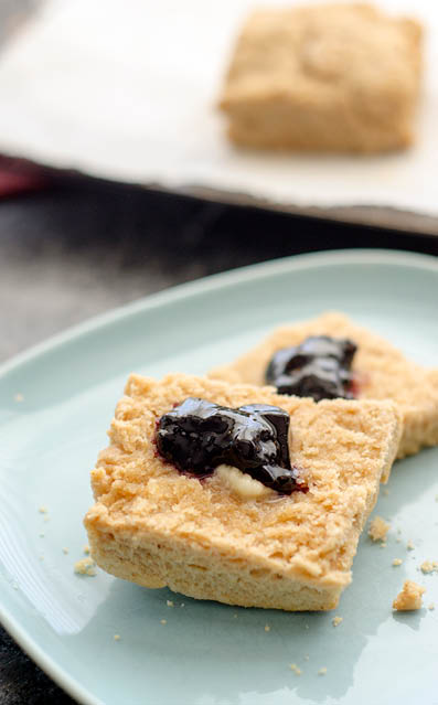 Square whole wheat biscuit  cut in half  on a blue plate  and topped with melting butter pat and a dollop of blackberry jam 