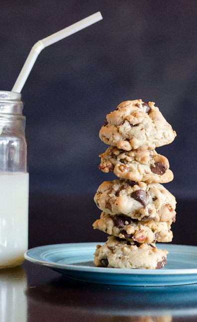 Stack of 5 chocolate chip cookies with pecans on a vintage blue Fiestaware plate  A mason jar of milk and a white straw are on the table next to the plate 