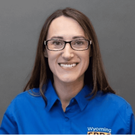 Devon Costa-Cargill: A headshot of Devon Costa-Cargill wearing a Wyoming-branded blue shirt, smiling warmly, set against a plain gray background.