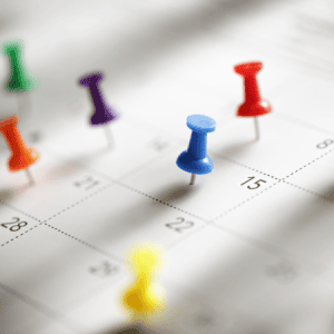 Calendar with colored pushpins: A close-up of a calendar with various colored pushpins marking specific dates, symbolizing the planning and scheduling of important events or deadlines.