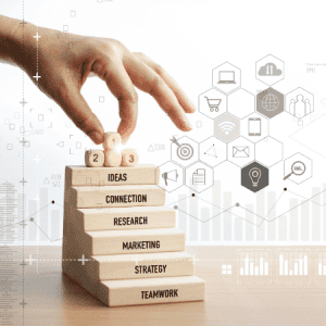 Hand stacking blocks with marketing concepts: A hand places wooden blocks labeled with marketing concepts like "Ideas," "Connection," "Research," "Marketing," "Strategy," and "Teamwork," representing the foundational steps in building a successful business.