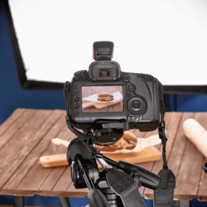 Camera setup for product photography: A professional camera on a tripod focused on a product setup on a wooden table with studio lighting in the background, demonstrating a product photography session.