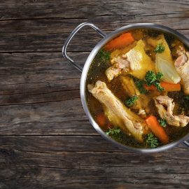 stock pot with broth, chicken, and vegetables on wood background