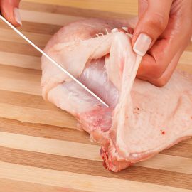 knife slicing through raw chicken breast