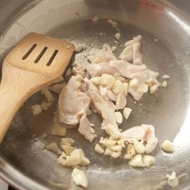 wood spoon stirring cooked chicken in metal pan