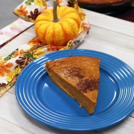 slice of pie on blue plate with tiny pumpkin and leafy ribbon in background