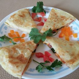 Quesadilla in 4 slices on white plate with tomato, pepper, and cilantro garnish.
