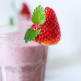 smoothie in clear glass gar with whole strawberry garnish and blurred background.