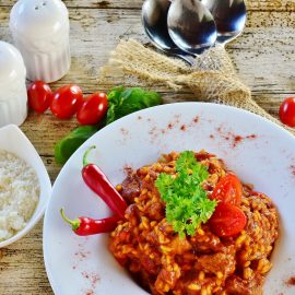 recipe garnished with tomato, parsley, chili with white rice side dish