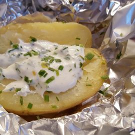 baked potato with sour cream and chives in tin foil