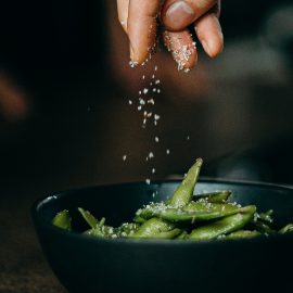 hand dropping spices on bowl of green beans