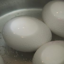 4 white eggs in metal pot with water about to boil