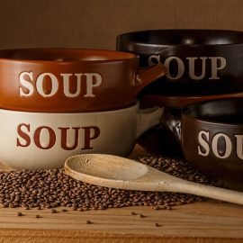 Four stacked bowls with engraved word "soup" and wooden spoon resting on dry beans
