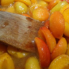 wooden spoon stirring peaches in sauce
