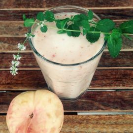 whole peach next to smoothie in clear glass topped with mint sprig