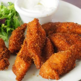 baked chicken strips with salad and dressing on a white plate
