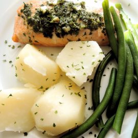 salmon topped with green sauce next to potatoes and green beans