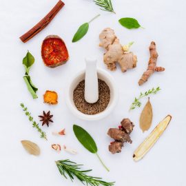 mortar and pestle with ground spice surrounded by whole spices such as rosemary, ginger, star anise, and cinnamon