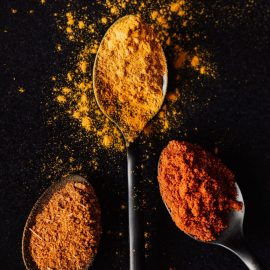 Three metal spoons with varied crushed spices on black background
