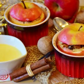 two baked apples in ramekins with cinnamon sticks