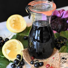 chokecherry gravy in glass bottle surrounded by lemons and berries