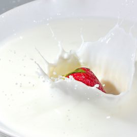 whole strawberry falling into bowl of yogurt