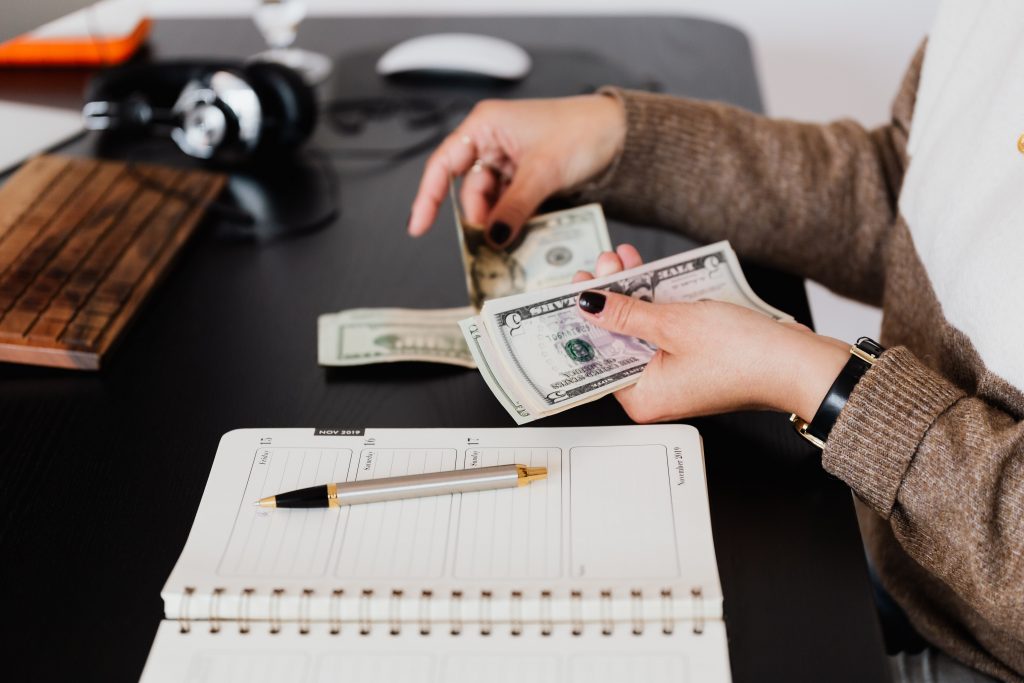 woman's hands holding money next to a notebook