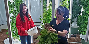 Two women standing next to vertical garden