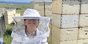 Child in bee hood in front of bee hives.