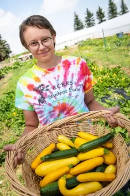 Acres Student Farm worker holding a basket of green and yellow squash.