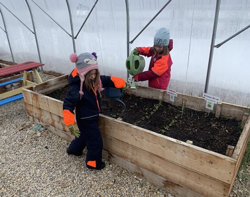 Kids watering plants in a greenhouse.