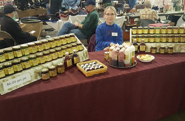 Woman sitting at a table with jars of homemade goods.
