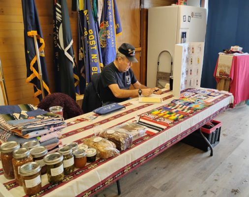 Man working at table with baked goods and crafts.