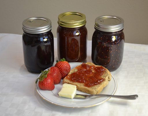Jars of jam with plate of toast and fresh fruit