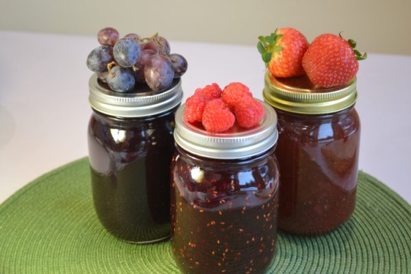 Jars of jam with fresh blueberries, raspberries, and strawberries