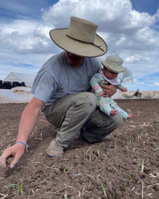 Man planting garden while holding baby.