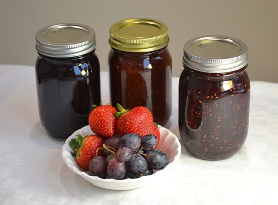 Jars of homemade jam and a bowl of fresh fruit