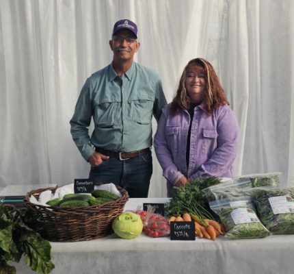 Two people standing behind a table with fresh produce.
