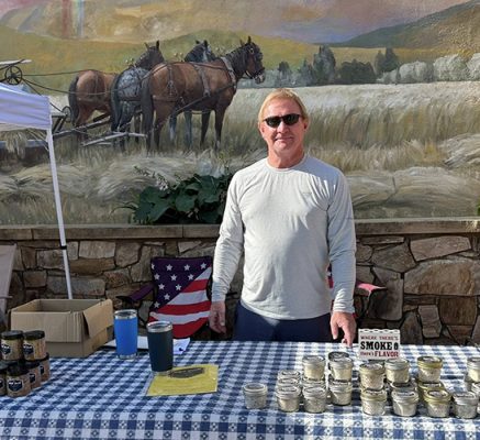 Man beside table with cans of smoked salts and sugars.